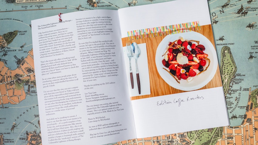 An opened zine showing text and a photo of a meal, laid ontop of a map of Sydney.