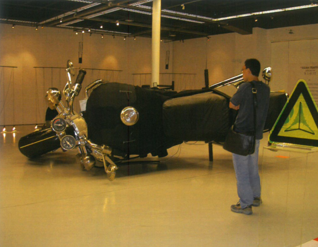 A gallery visitor observing an artwork of a large motorcycle resting on its side as part of the Beijing exhibition "Asian Traffic."