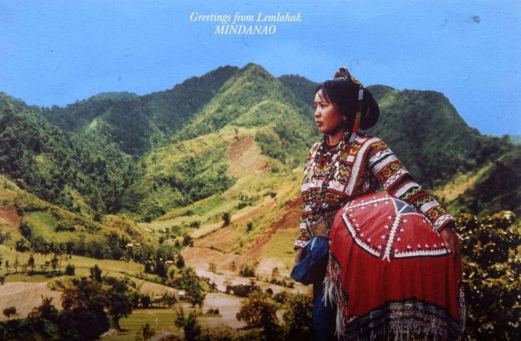 Profile of a Mindanao woman in traditional clothing with green hills and a blue sky in the background