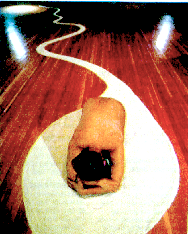 A photo of a naked figure sitting on the floor with head rested on their arms.