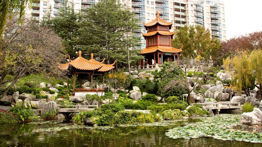 A landscape photo of the Chinese Garden of Friendship, depicting a green pond, rocks, and greenery with two red and orange pagodas in the distance.