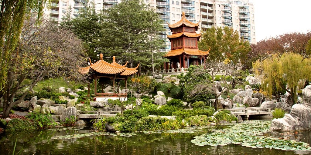 A landscape photo of the Chinese Garden of Friendship, depicting a green pond, rocks, and greenery with two red and orange pagodas in the distance.