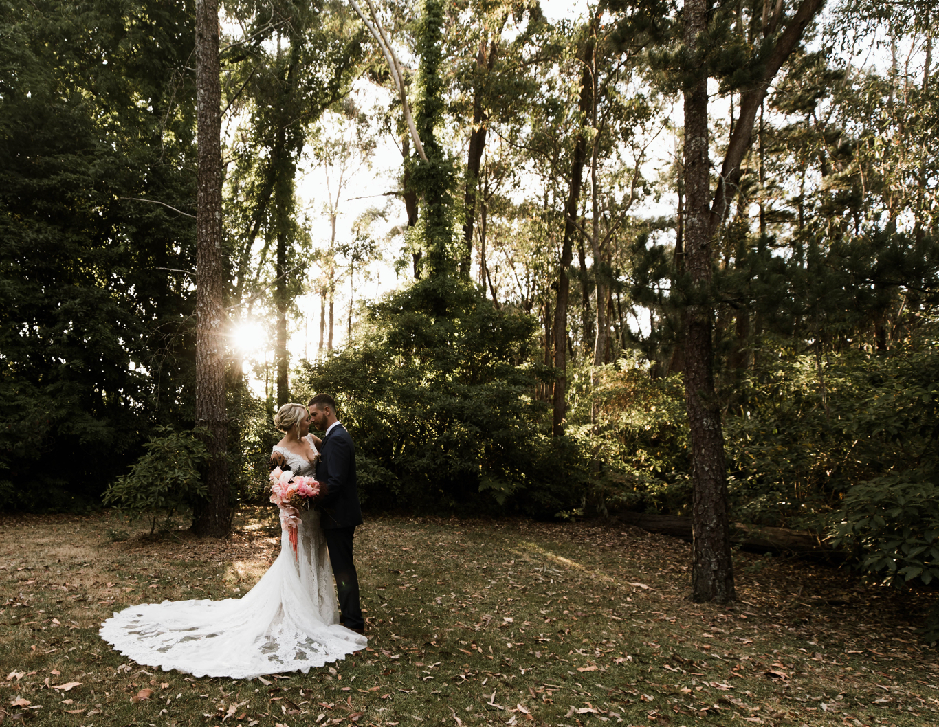Wedding couple embrace amongst sunlit bushland.