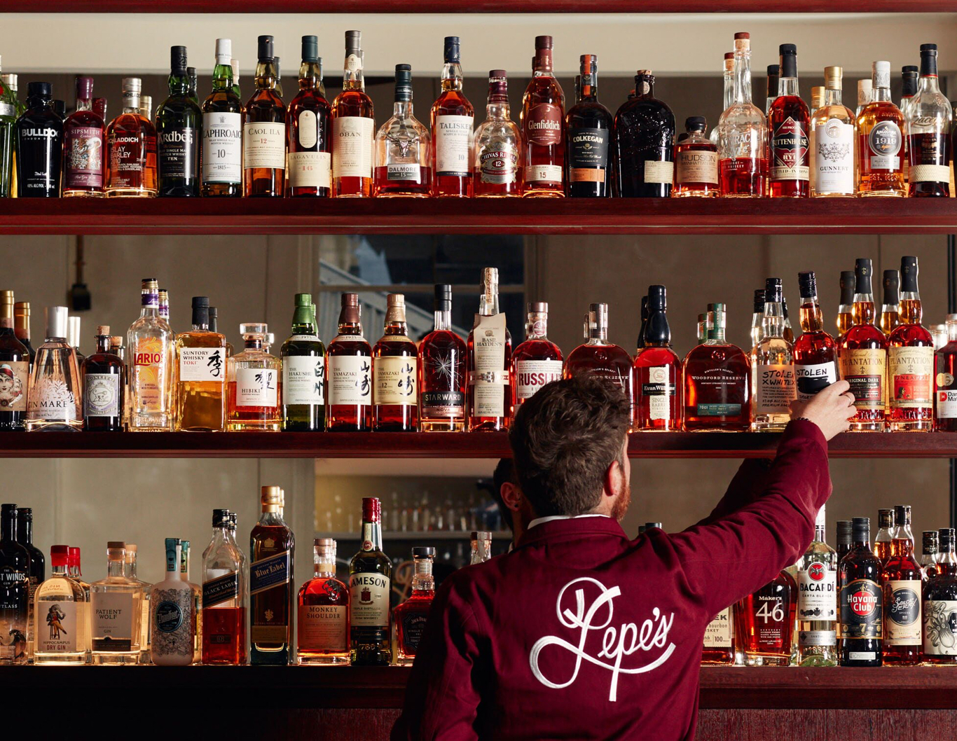 Bartender reaching for spirits on a mirrored bar.