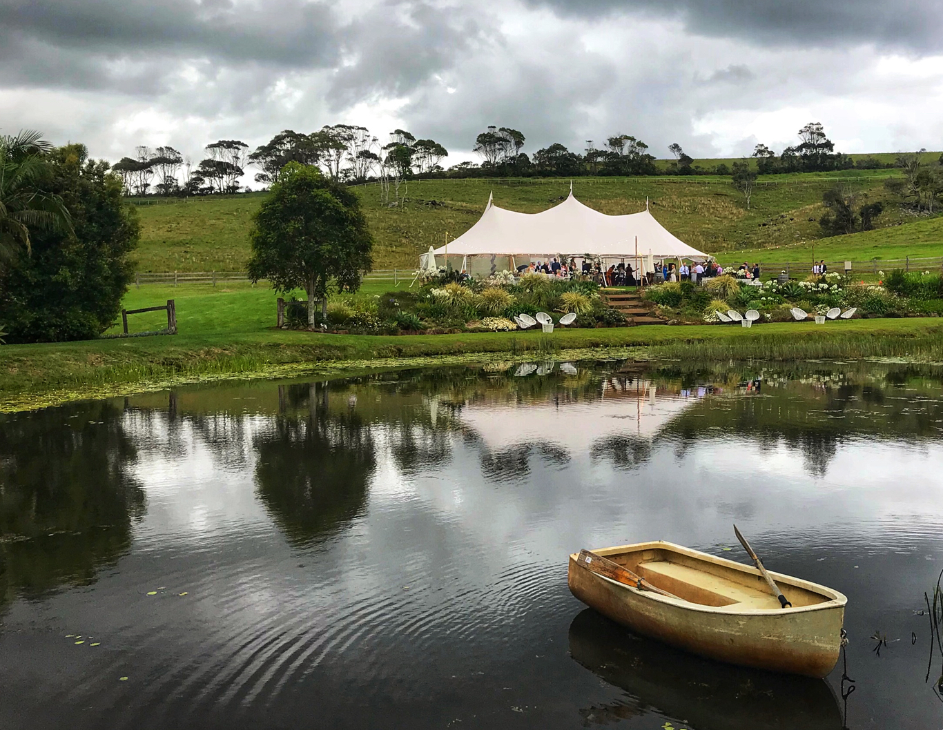 A boat floating on a lake, with wedding reception tipi in the background.