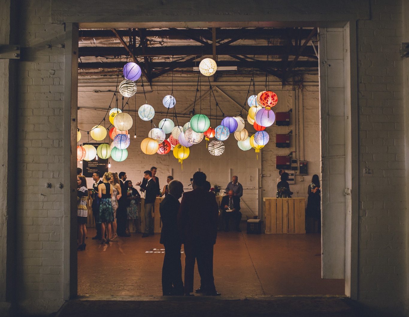 Weddings guests under light installation inside a barn.