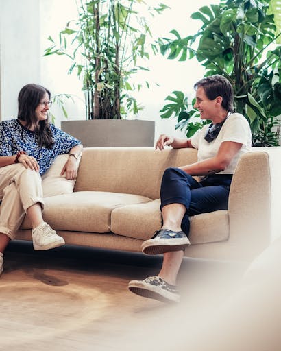 Two women talking sitting on a sofa shown sideways