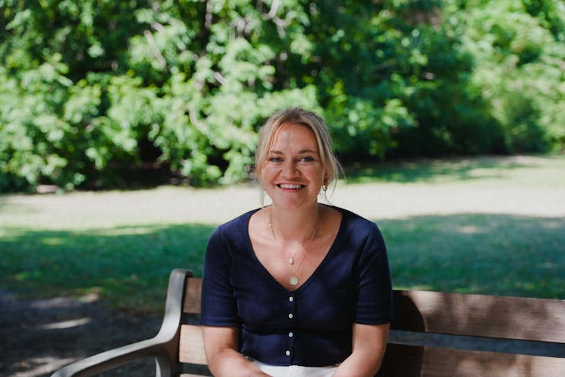 Woman looking into the camera sitting on a bench in the park smiling