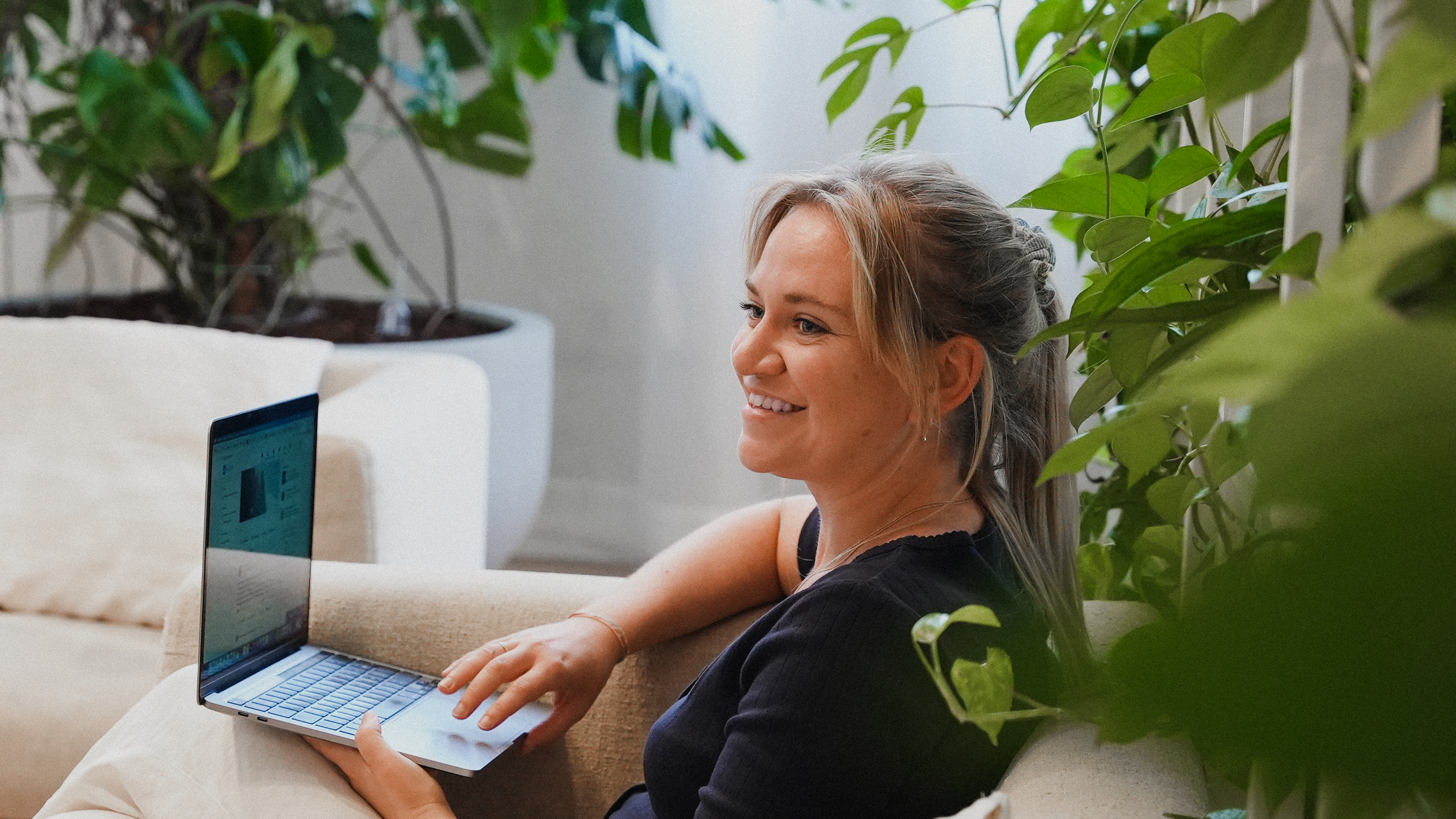 Woman smiling sideways sitting in a couch behind a laptop