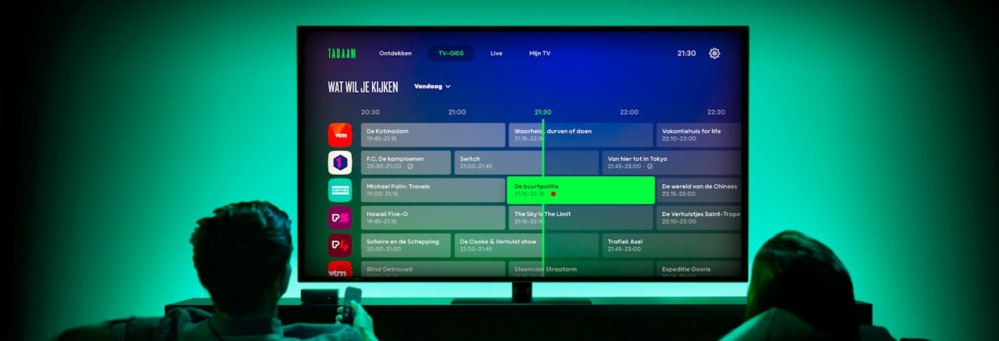 Two people watching a tv showing the Tadaam interface