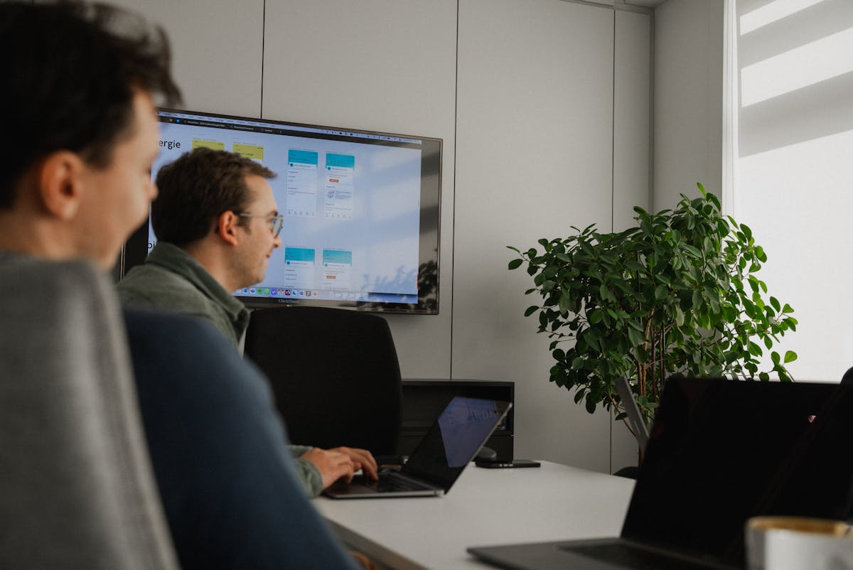 Two people with laptops sitting in a meeting room in front of a tv screen
