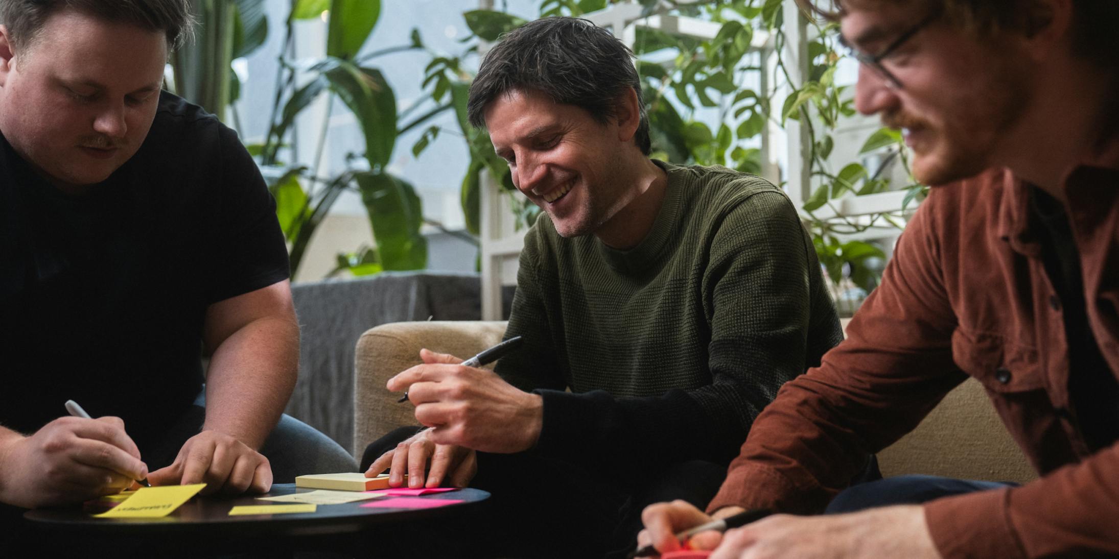 Three Craftzing colleagues writing on post-its and smiling