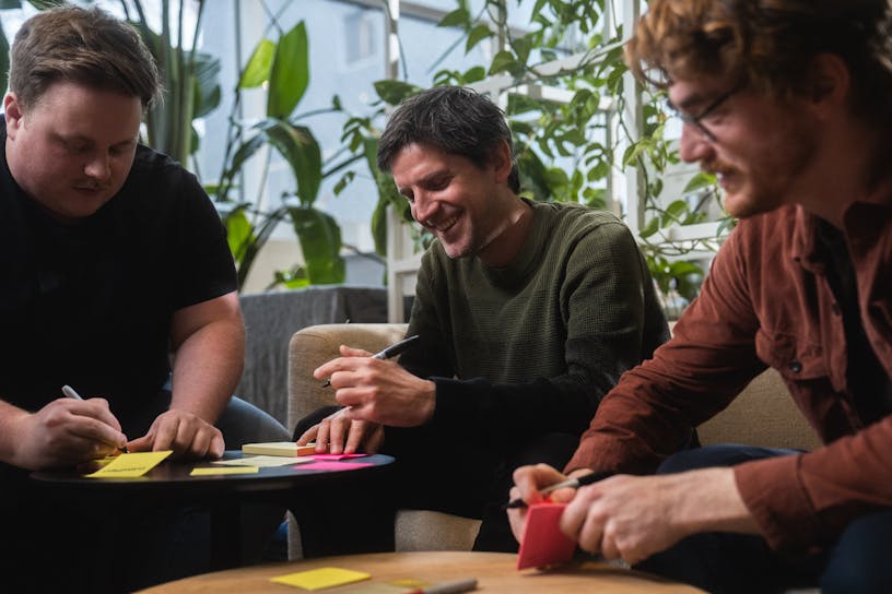 Three Craftzing colleagues writing on post-its and smiling