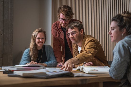 2 men and 2 women sitting at a desk going through books on the table.