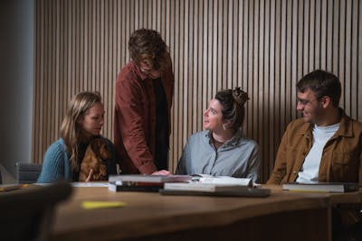 2 woman and 2 men of the Craftzing data team, 3 of them sitting at a table, the other one standing and explaining something.