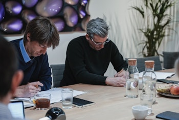 Two men in a meeting room taking notes during a workshop