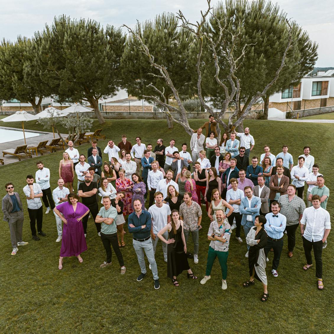 The entire Craftzing team standing side by side in the garden of a Portuguese resort where the Craftzing Unplug took place. In the background trees, a swimming pool and holiday homes.
