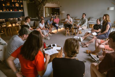 Group of Craftzing colleagues sitting on stools in a circle listening to someone who's explaining something during a workshop