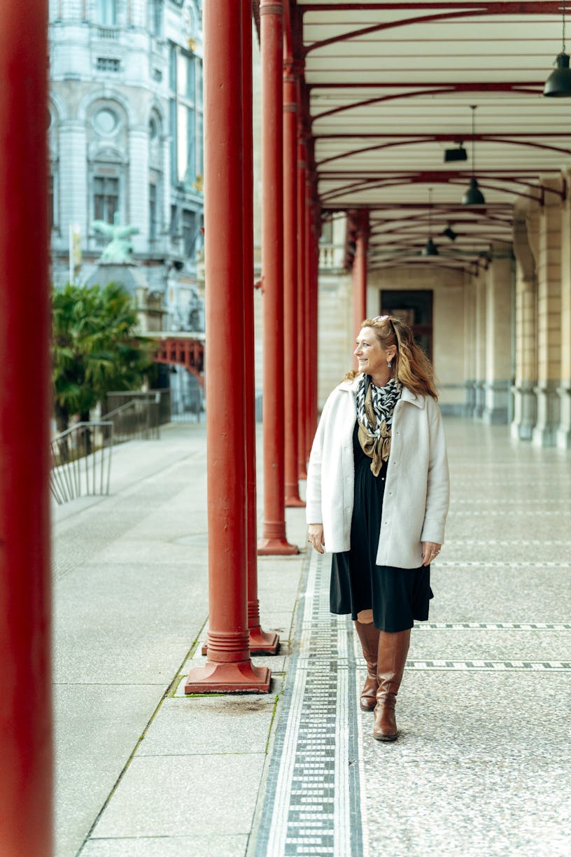 Business Partner Financial Services Hilde Van den Dungen wearing a dark dress, a beige sweater and a scarf with leopard print. She's walking towards the camera while looking sideway's
