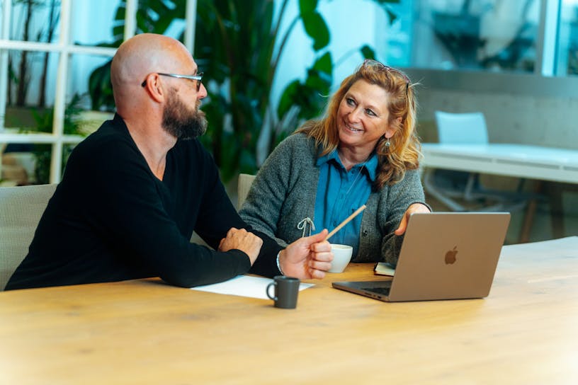 Business Partner Financial Services Hilde Van den Dungen discussing something with her colleague Kenneth Roelandt at a desk in the Craftzing Antwerp office