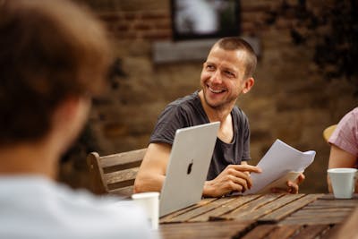 A man holds a piece of paper and smiles at someone next to him who is outside the frame.