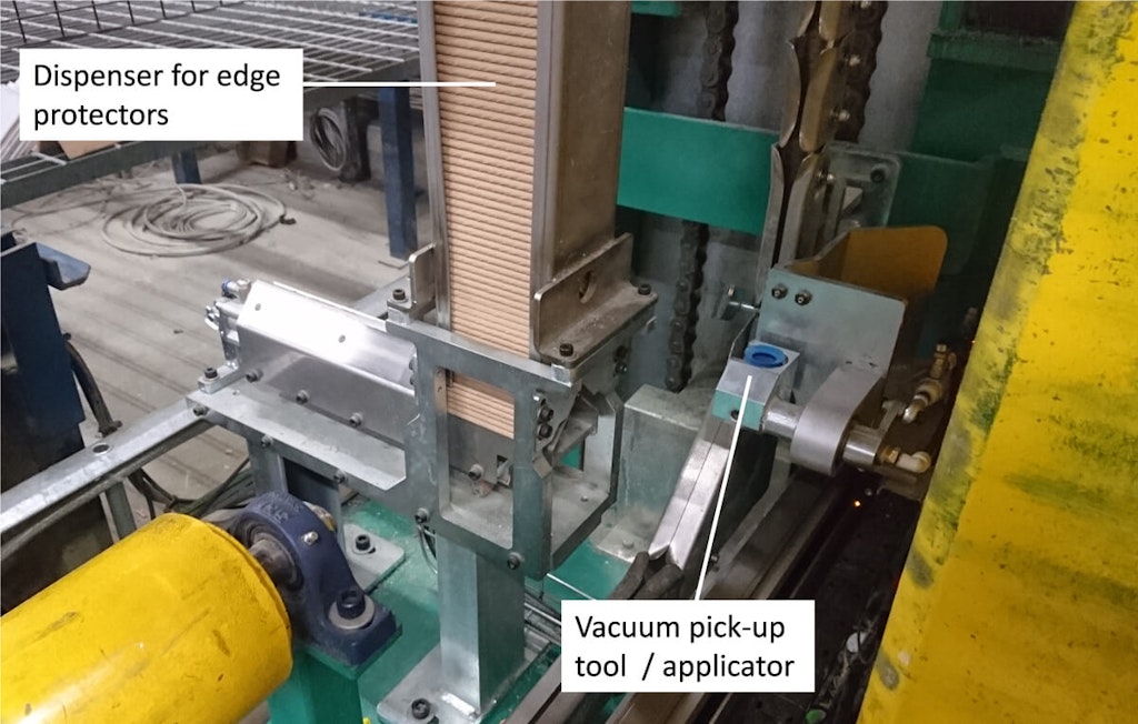 Figure 5. A pneumatic linear feeding device pushes the edge applicator (stored in the dispenser) to the right in the picture where the vacuum pick-up tool is being rotated towards the viewer to pick up the edge protector. Then the pick-up/applicator positions the edge protection on the timber package while it is being strapped.