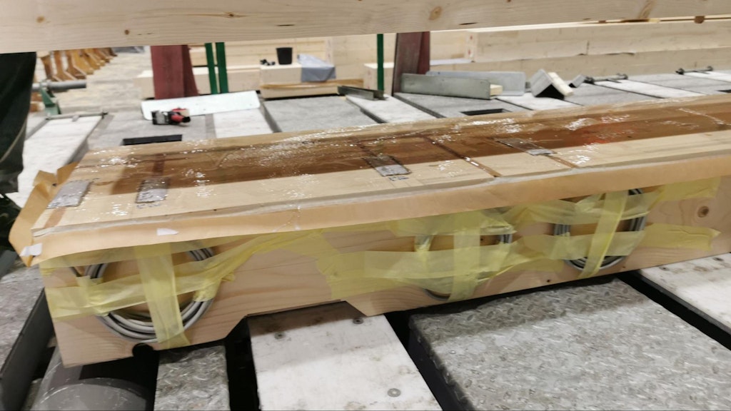 The process of gluing the two wooden cross-beam halves in the block press - note that a distinct rubber covers the strain gauges against humidity. The engineers routed the inside cables around the later-inserted threaded rods to prevent a collision.
