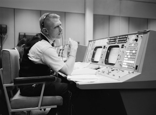 Eugene F. Kranz, flight director, is shown at his console on May 30, 1965, in the Mission Operations Control Room at Mission Control in Houston, preparing for a Gemini-Titan IV mission: public domain, NASA Photo S-65-22203.