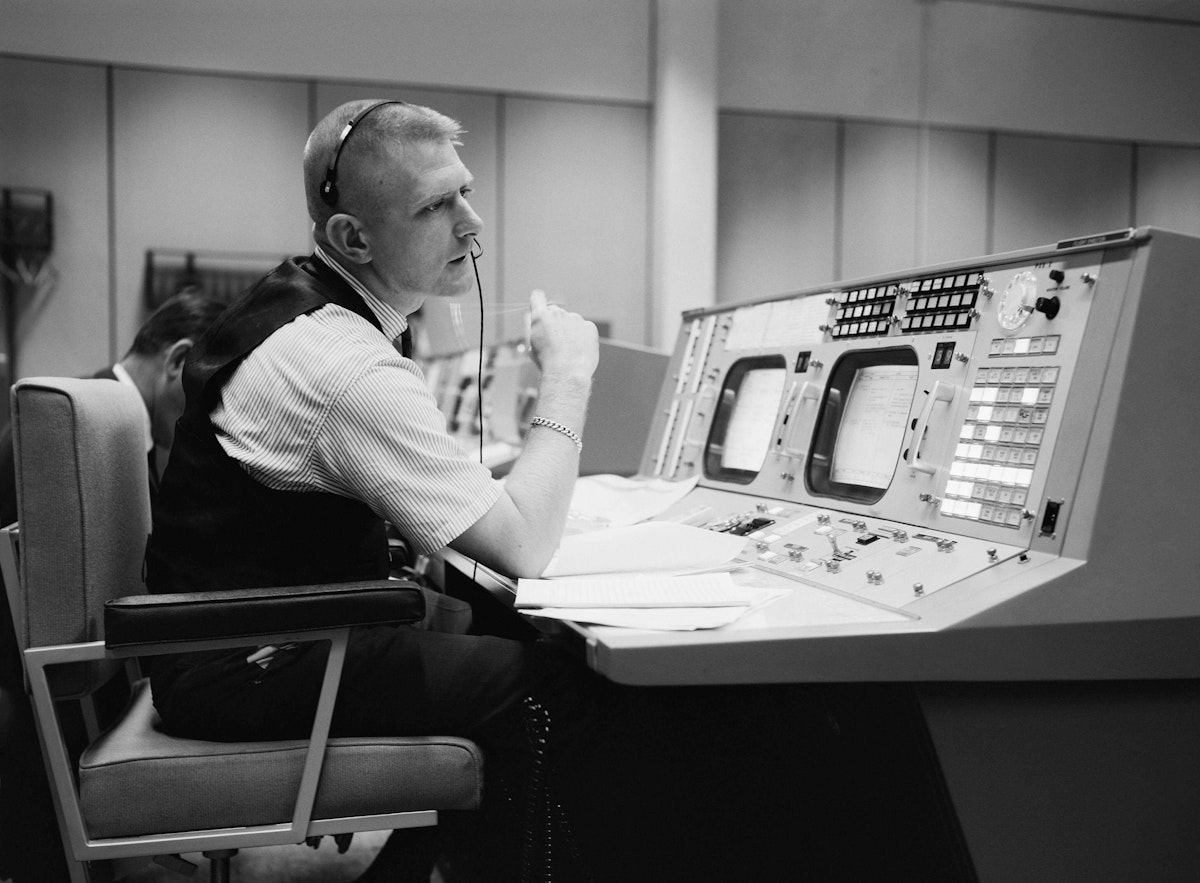 Eugene F. Kranz, flight director, is shown at his console on May 30, 1965, in the Mission Operations Control Room at Mission Control in Houston, preparing for a Gemini-Titan IV mission: public domain, NASA Photo S-65-22203.