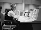 Eugene F. Kranz, flight director, is shown at his console on May 30, 1965, in the Mission Operations Control Room at Mission Control in Houston, preparing for a Gemini-Titan IV mission: public domain, NASA Photo S-65-22203.