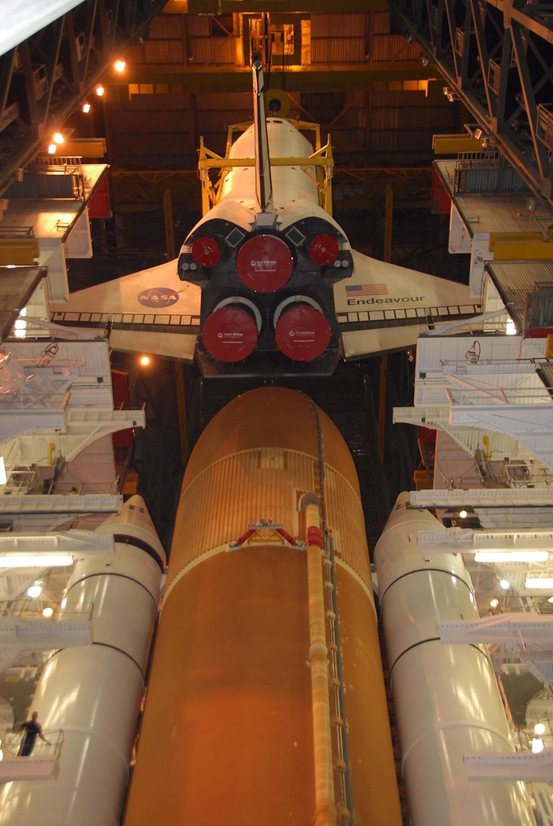 The Endeavour orbiter is lowered toward the stack on the mobile launcher platform.–Photos by NASA. The Endeavour orbiter is lowered toward the stack on the mobile launcher platform.–Photos by NASA.