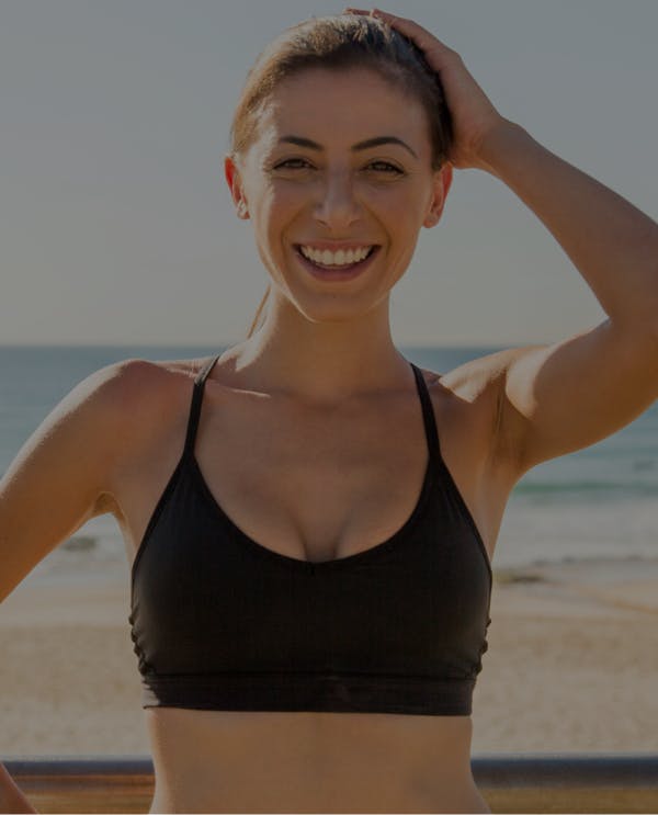 Woman wearing a sports bra, smiling outside at the beach