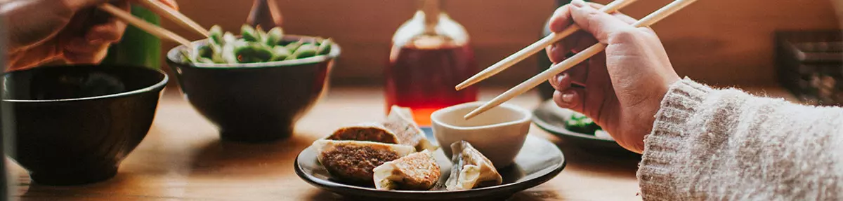 hands holding chopsticks, plate of gyoza and bowl of edamame