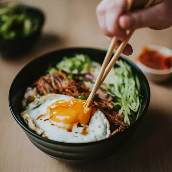 chopsticks breaking the yolk of a fried egg in the grilled duck donburi