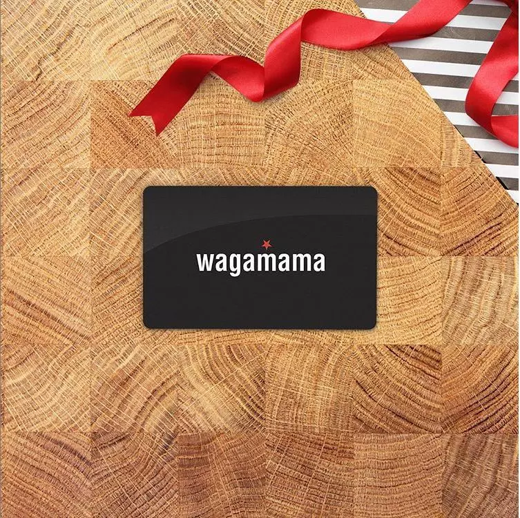 wagamama gift card on a wooden background. black and white striped wrapping paper and a red ribbon are in the top right hand corner