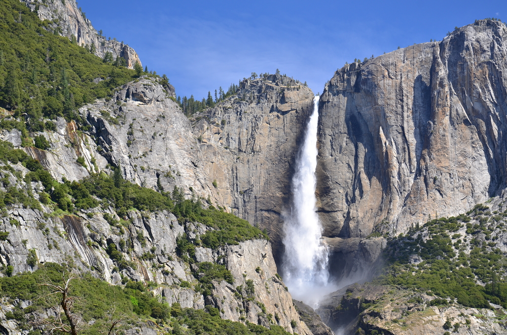 A waterfall flowing over a rock face into the valley below on a sunny spring day.