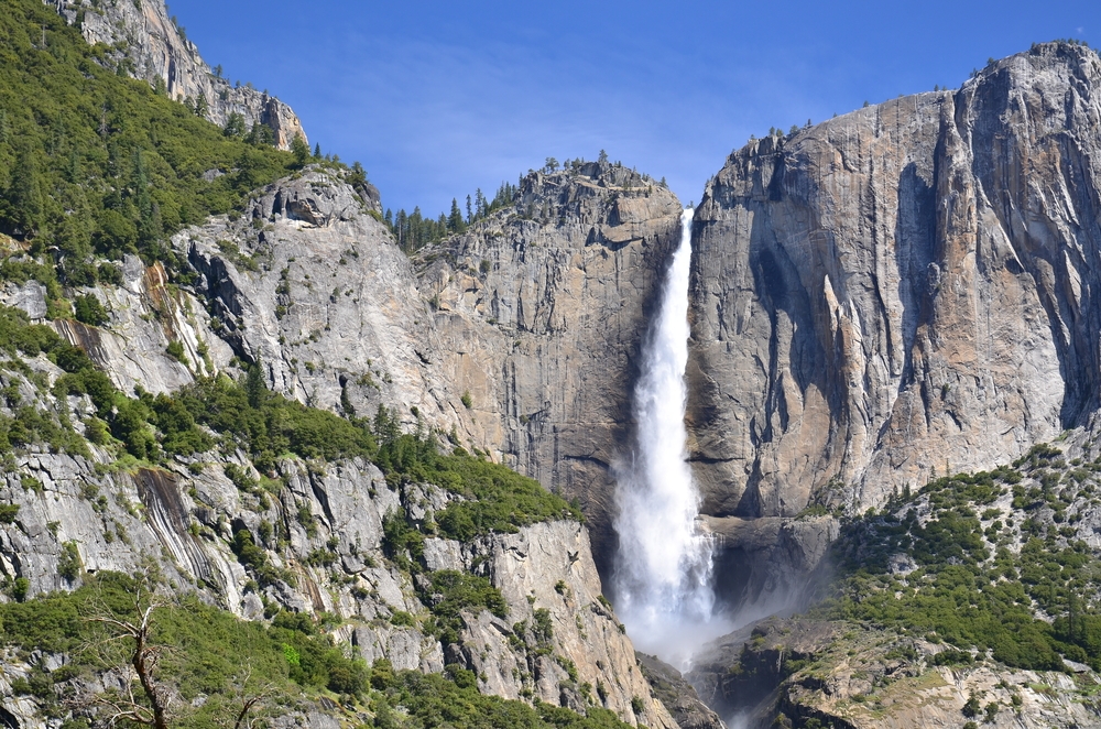 A waterfall flowing over a rock face into the valley below on a sunny spring day.