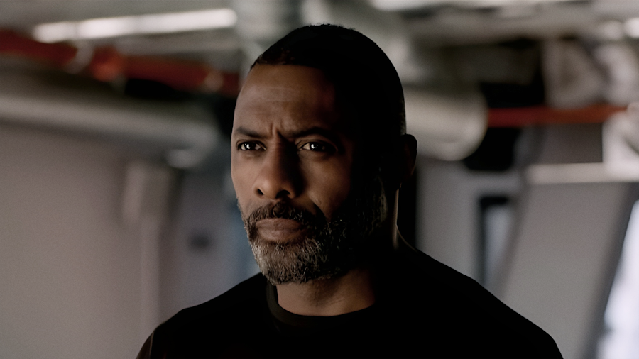Idris Elba standing atop a skyscraper in San Francisco, looking at how finding gold ore transformed the Californian skyline.