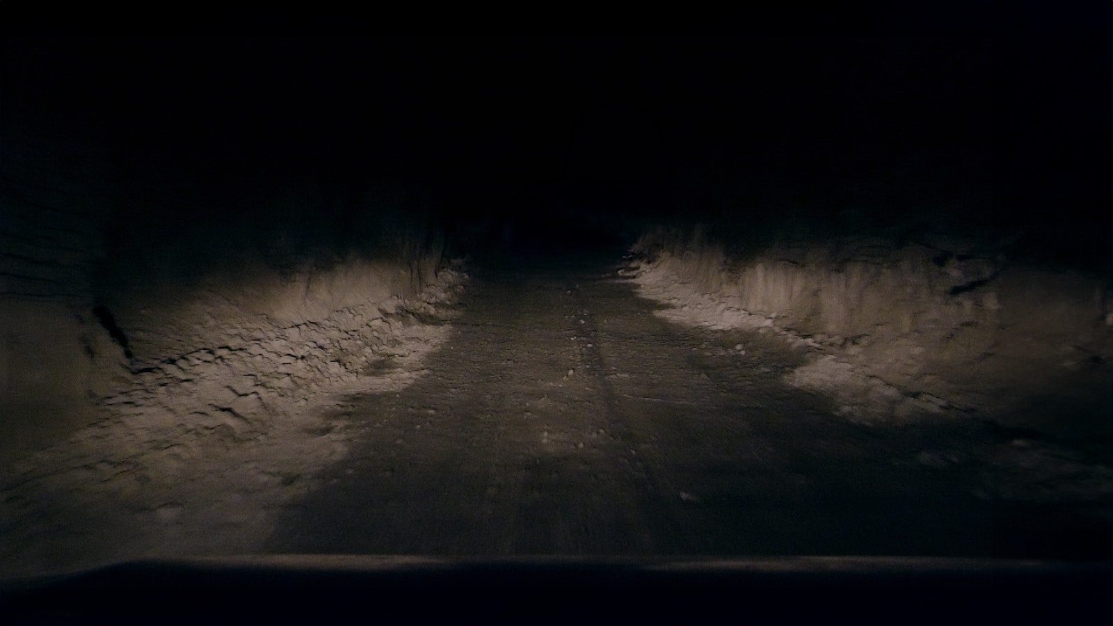 Deep underground a mining truck’s lights break through the pitch black, revealing grey rocky roads.