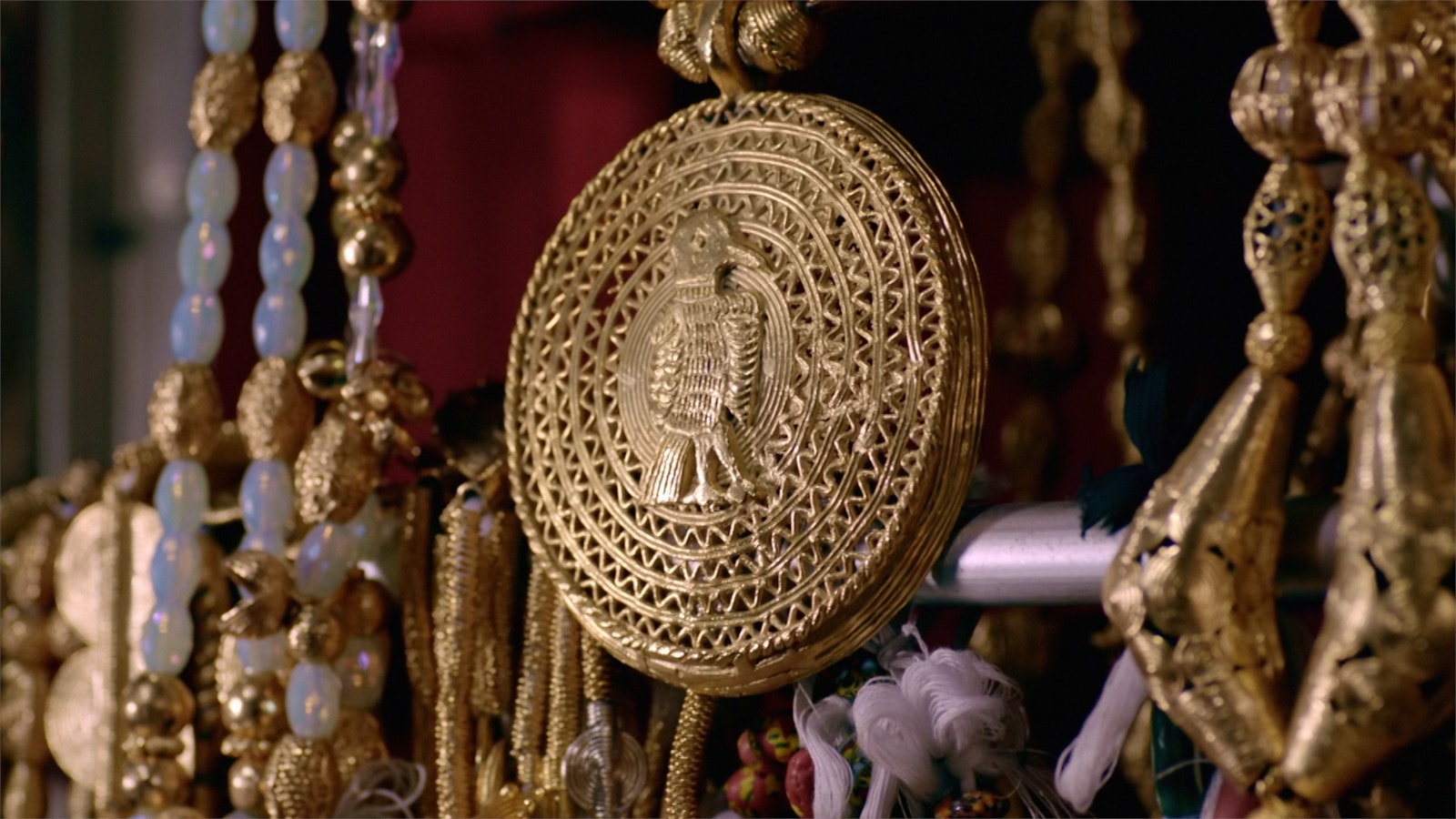 A large, circular gold pendant, with ornate details and a motif at the centre, hangs in a shop alongside other ornaments.