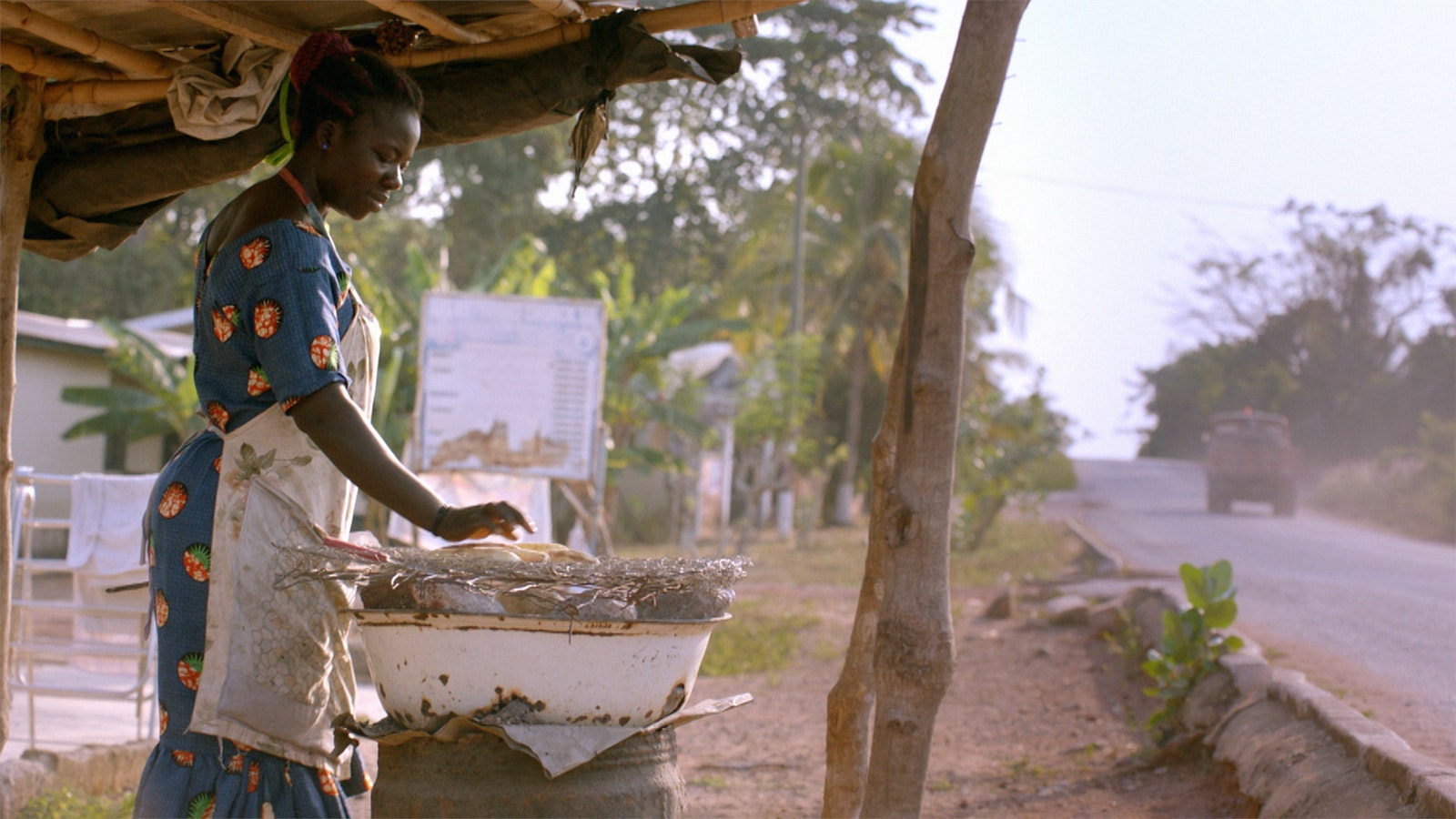 A local business woman prepares food at her restaurant, she tends to food under a gazebo-type structure.