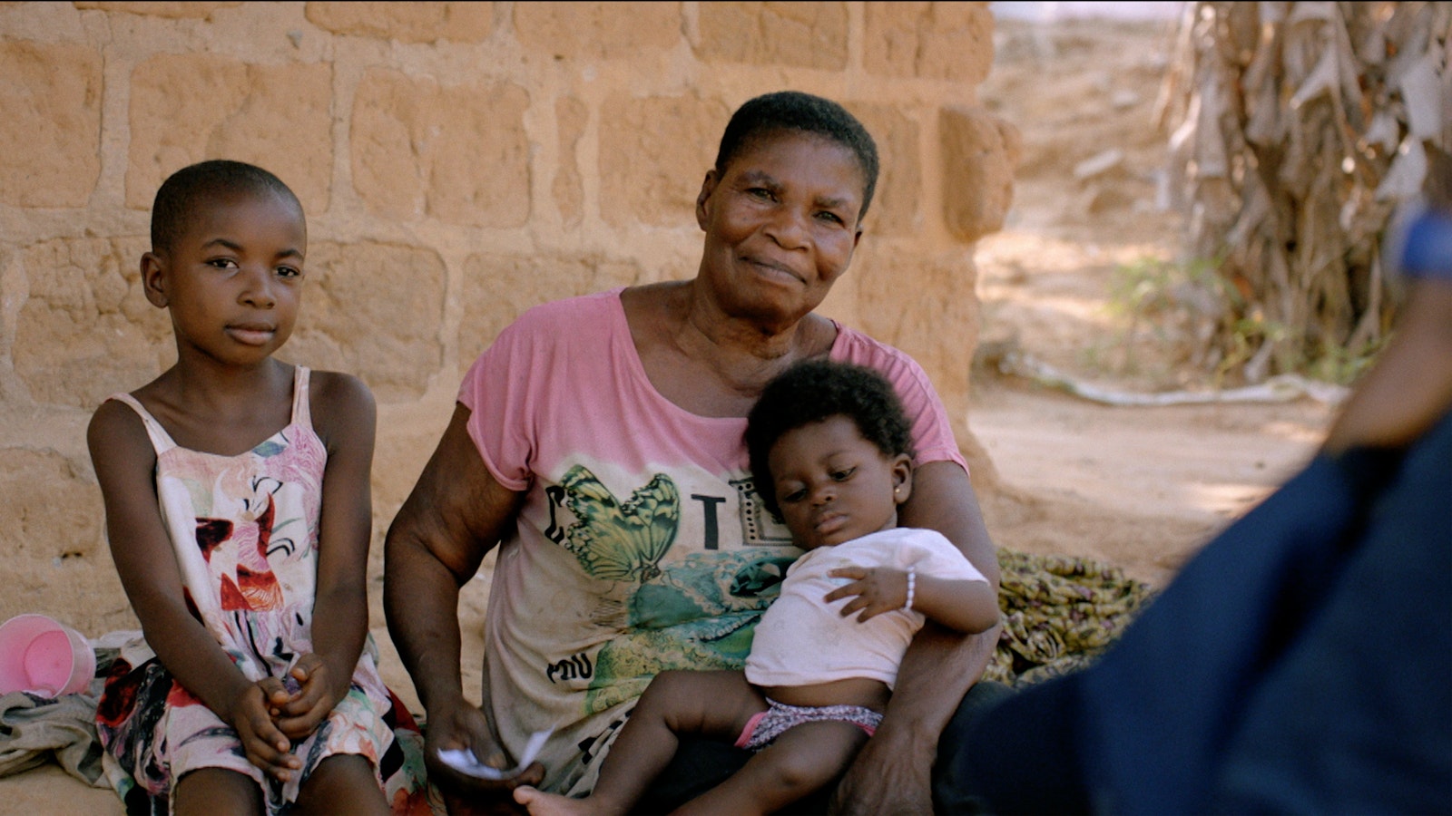 A woman sits with her two children outside the brick wall of her home, which has been treated by the programme.