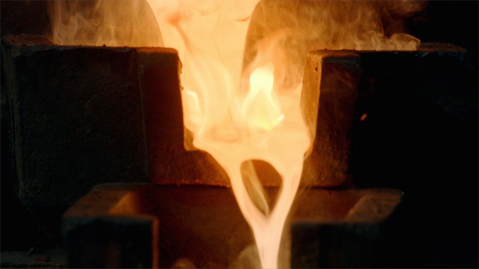 A rich golden-orange lava colour, liquid gold pours from the mouth of a furnace, through a series of moulds.