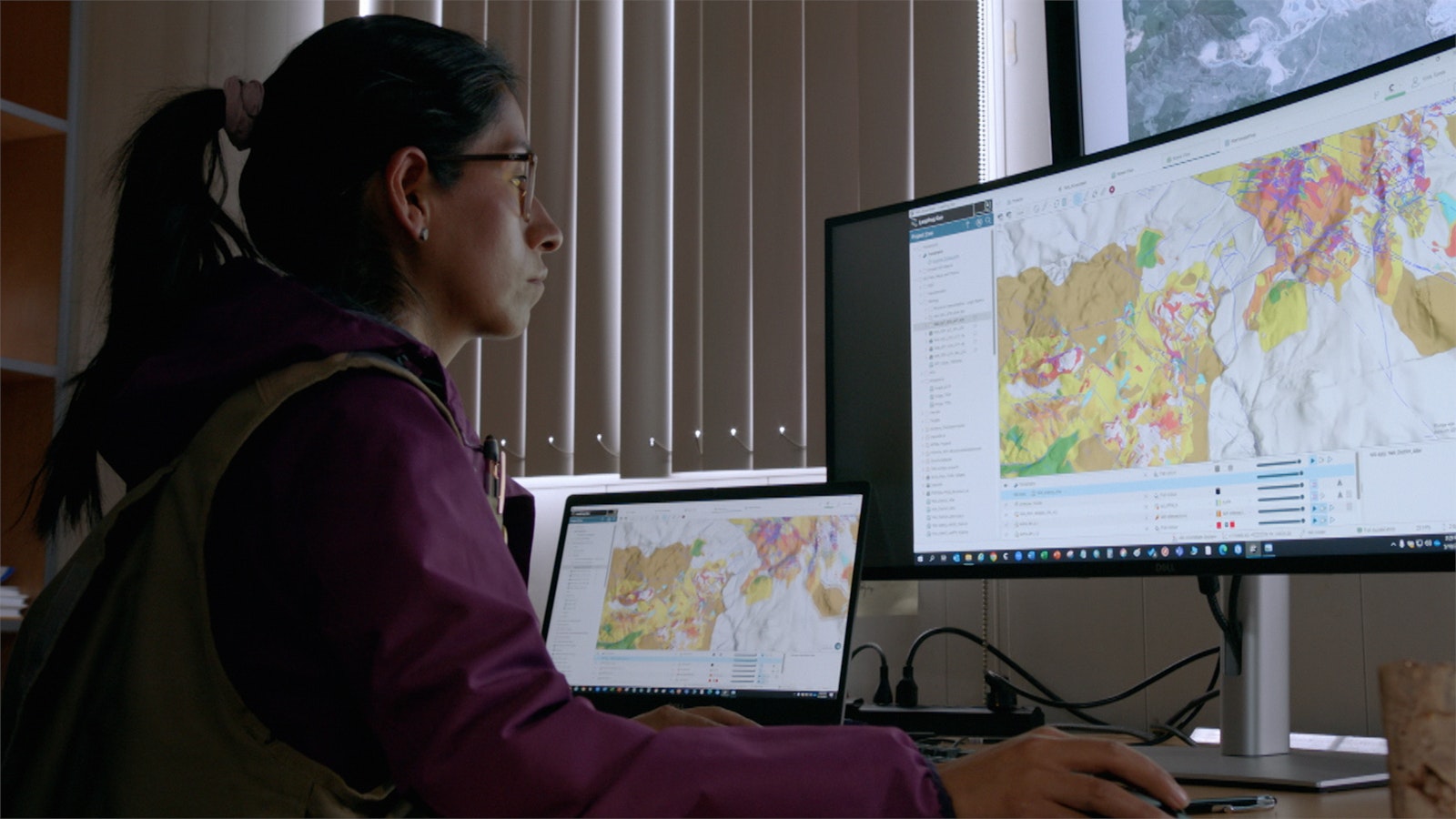 Denisse Quispe sits in front of a large computer screen reviewing a map of colourful satellite data.