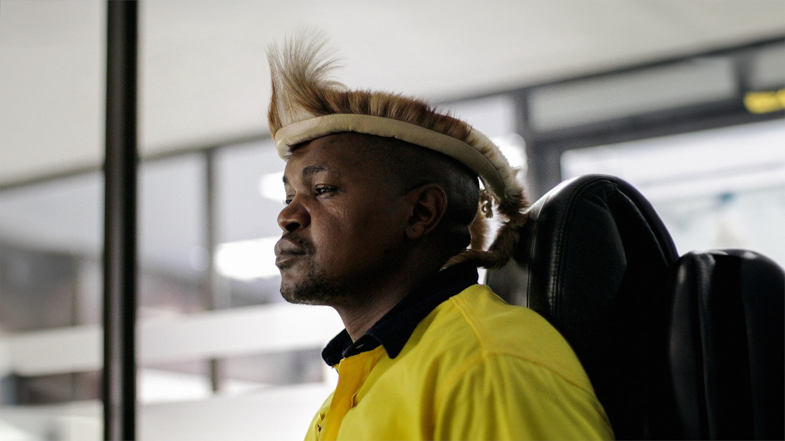 A modern-day African mine worker sits in a chair at South Africa’s South Deep Mine, he wears a traditional headdress.