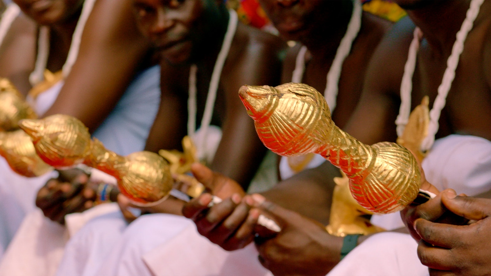 The king's chiefs line up in preparation for meeting the king. They wear gold-adorned headdresses and gold-hilted swords