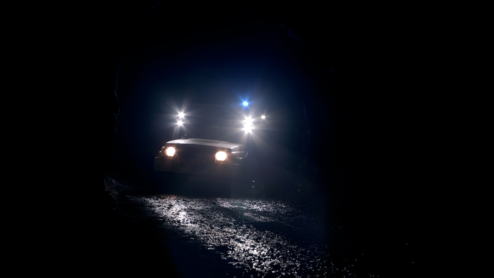 Inside a deep mine tunnel-road the headlights of a mining truck pierce the darkness.