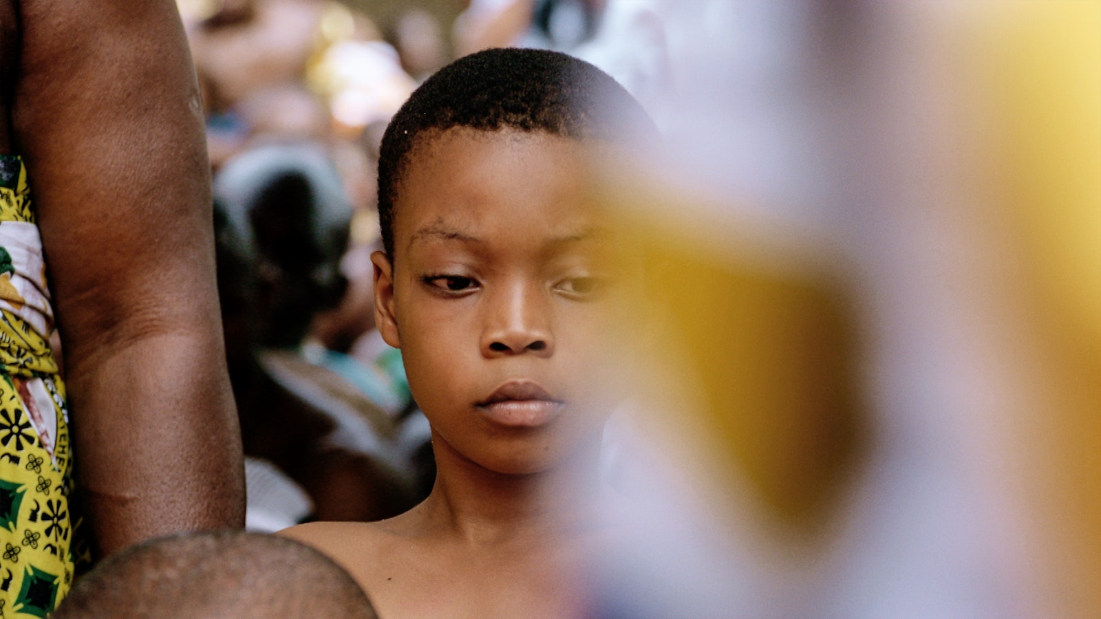 Backed by a crowd of people, a young boy attends the Ashanti nation's cultural celebration.
