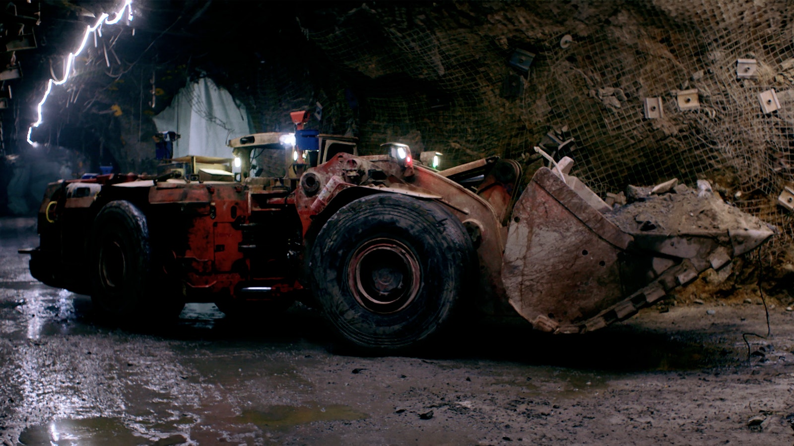A large yellow mining truck with huge black wheels navigates the mine tunnel, with no human driver in the cab.