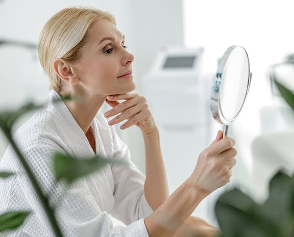 Woman looking in mirror after receiving thread lift